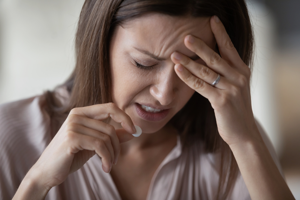 A woman having a headache while holding a Xanax pill i her hand.