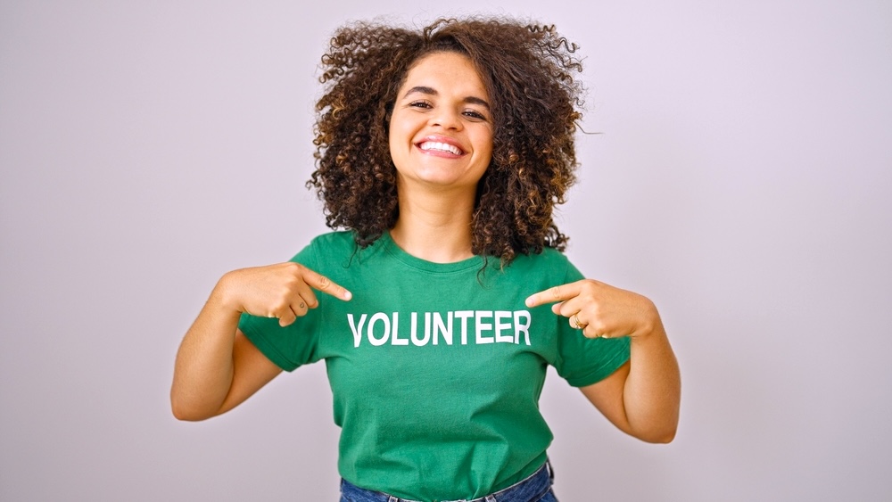 A hispanic woman in addiction recovery pointing to volunteer uniform smiling