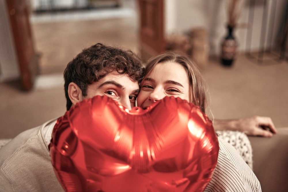 Couple hiding behind a red heart balloon