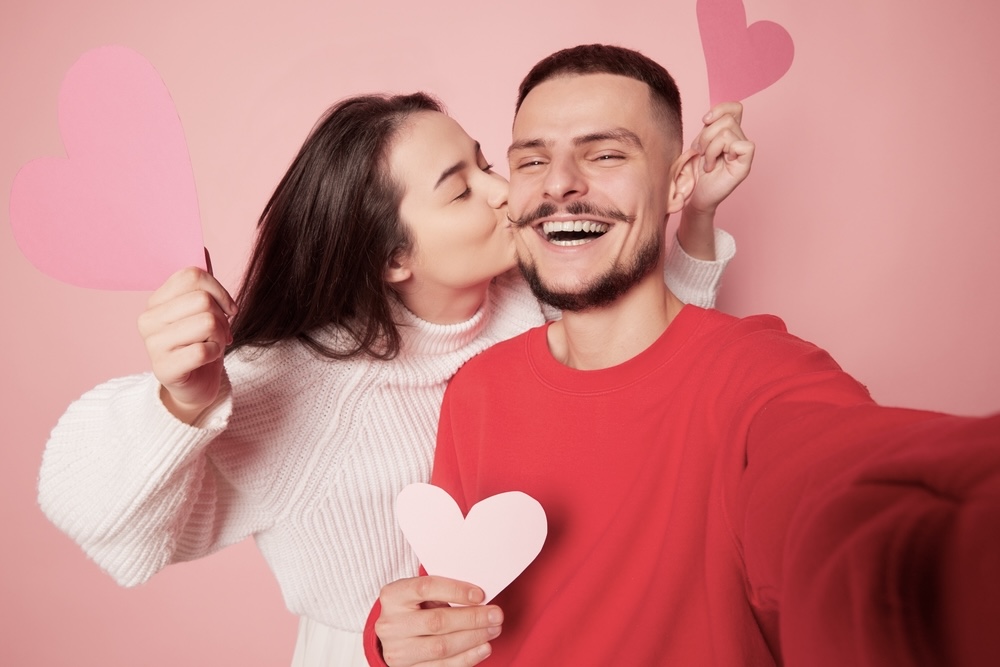 A happy couple kissing while holding heart paper shape