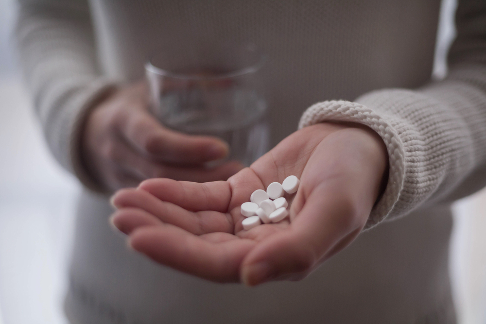 Close-up view photo of female hands holding Dilaudid pills and glass of water.